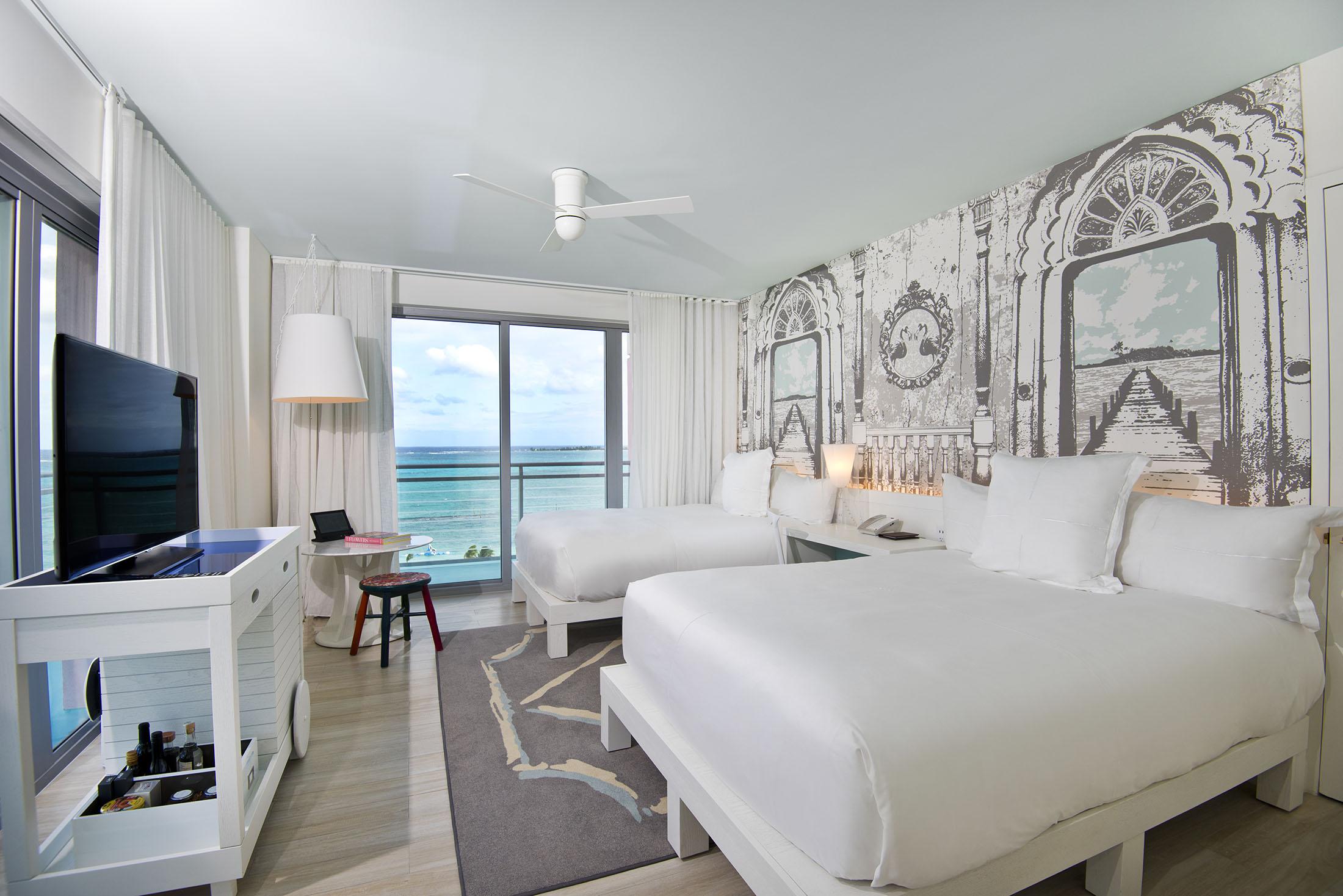 2 개의 침대가있는 호텔 침실과 바다가 내려다 보이는 파티오 창문이 있습니다.