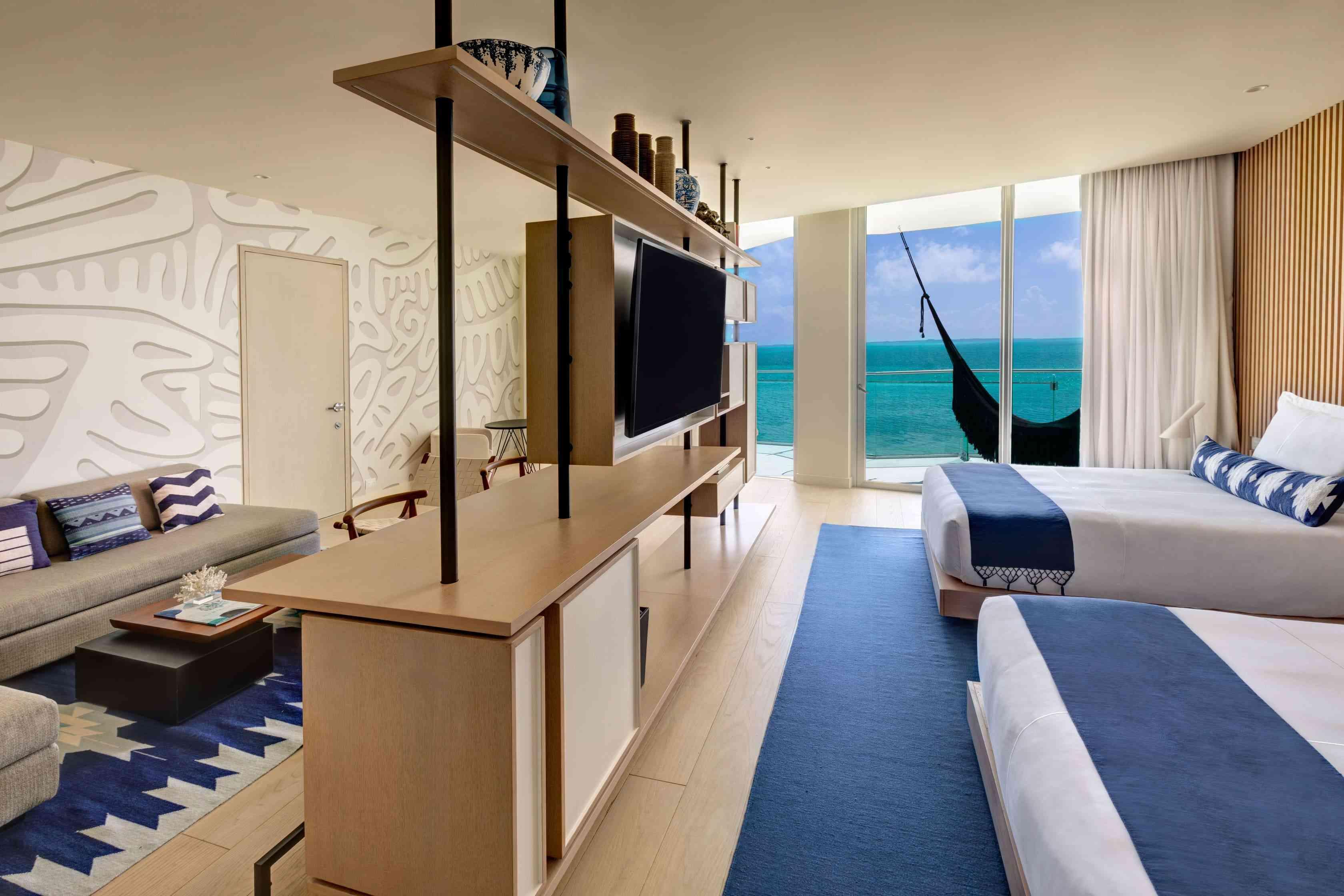 더블 침대 2개, TV, 침실과 거실을 분리하는 책상, 바다가 내려다보이는 해먹이 있는 발코니가 있는 디럭스 오션 프런트 1베드룸 스위트의 모습